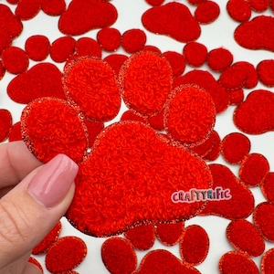 May include: Red fuzzy paw print fabric patches with a glittery outline. The patches are arranged in a random pattern on a white background.