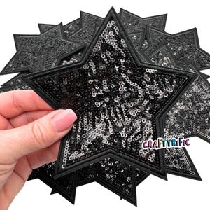 Puede incluir: Parches de estrella de lentejuelas negras con borde negro. Los parches en forma de estrella están cubiertos de lentejuelas negras brillantes. Una mano sostiene algunos de los parches. El texto "CRAFTYRIFIC" es visible en uno de los parches.