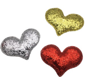 May include: Three heart-shaped decorations made of sparkly fabric. The hearts are red, silver, and gold.