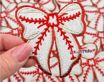 May include: White and red embroidered baseball-themed bow with a glittery finish. The bow is shaped like a baseball with red stitching.