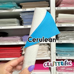 May include: A roll of white textured material with a cerulean blue backing is displayed. The word "Cerulean" is written on the image. The background shows shelves with various colored papers, including pink, teal, and purple.