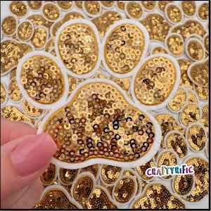 May include: A gold glitter paw print applique with a white felt border. The applique is surrounded by other gold glitter paw prints.
