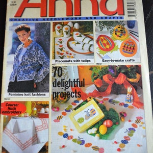 May include: A magazine cover for Anna, a publication focused on creative needlework and crafts. The cover features a woman wearing a blue and white patterned sweater, a close-up of a colorful embroidered design, and a variety of Easter-themed crafts, including placemats with tulips, easy-to-make crafts, and festive decorating ideas.