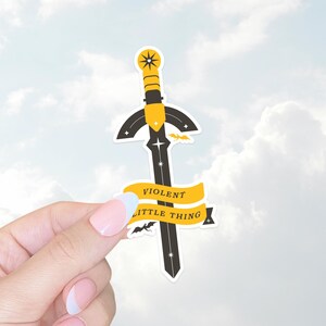 Peut inclure: Un autocollant noir et jaune avec une épée et le texte "VIOLENT LITTLE THING".