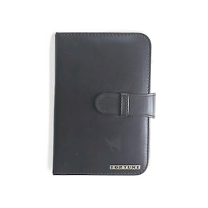 May include: A dark grey leather-effect wallet with a buckle fastening. The word "FORTUNE" is printed in silver letters at the bottom right corner. The wallet is rectangular and has a smooth surface.