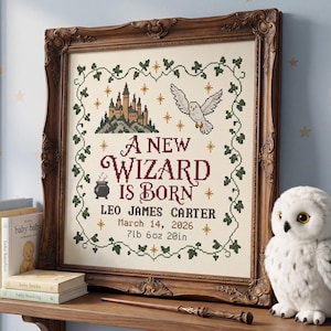 May include: A framed cross-stitch sampler featuring a castle, an owl, and a cauldron with the text A NEW WIZARD IS BORN, LEO JAMES CARTER, March 14, 2026, 7lb 6oz 20in, surrounded by a green vine border and gold stars on a cream fabric background.
