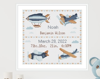 May include: A framed cross-stitch design with a blue and white airplane theme. The design includes the name "Noah Benjamin Wilson", the date "March 28, 2022", and the birth stats "7lbs. 10oz. 21in. 6:30PM".