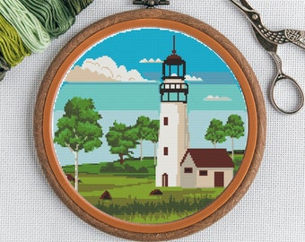 May include: A completed cross-stitch embroidery project depicting a white lighthouse with a brown roof, surrounded by green trees and a blue ocean. The embroidery is framed in a brown wooden hoop.