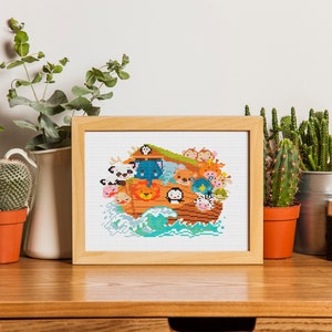 May include: A framed cross-stitch design featuring a cartoon Noah's Ark with various animals on board. The ark is brown with a blue roof and is surrounded by blue waves. The animals are all smiling and have different colors and patterns.