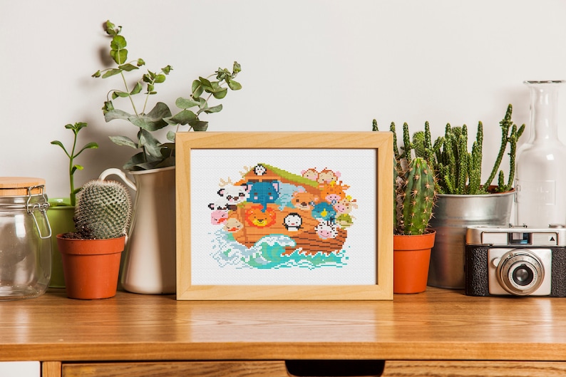 May include: A framed cross-stitch design featuring a cartoon Noah's Ark with various animals on board. The ark is brown with a blue roof and is surrounded by blue waves. The animals are all smiling and have different colors and patterns.