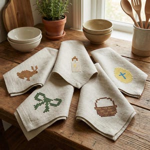 May include: A set of five beige linen napkins with embroidered Easter-themed designs. The designs include a brown bunny, a green bow, a candle, a yellow egg with a blue cross, and a brown basket. The napkins are arranged on a wooden surface.