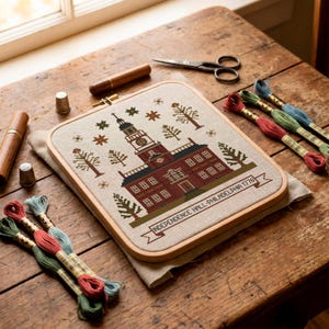 May include: A cross-stitch of Independence Hall in Philadelphia, Pennsylvania, in a wooden embroidery hoop. The design features a detailed depiction of the building with trees and stars. Colorful embroidery floss, scissors, and other sewing tools are arranged around the hoop.