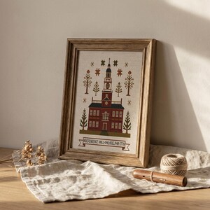 May include: A framed cross-stitch of Independence Hall in Philadelphia, Pennsylvania, with a wooden frame. The building is red brick with a white clock tower. The text "INDEPENDENCE HALL-PHILADELPHIA 1776" is below the building.