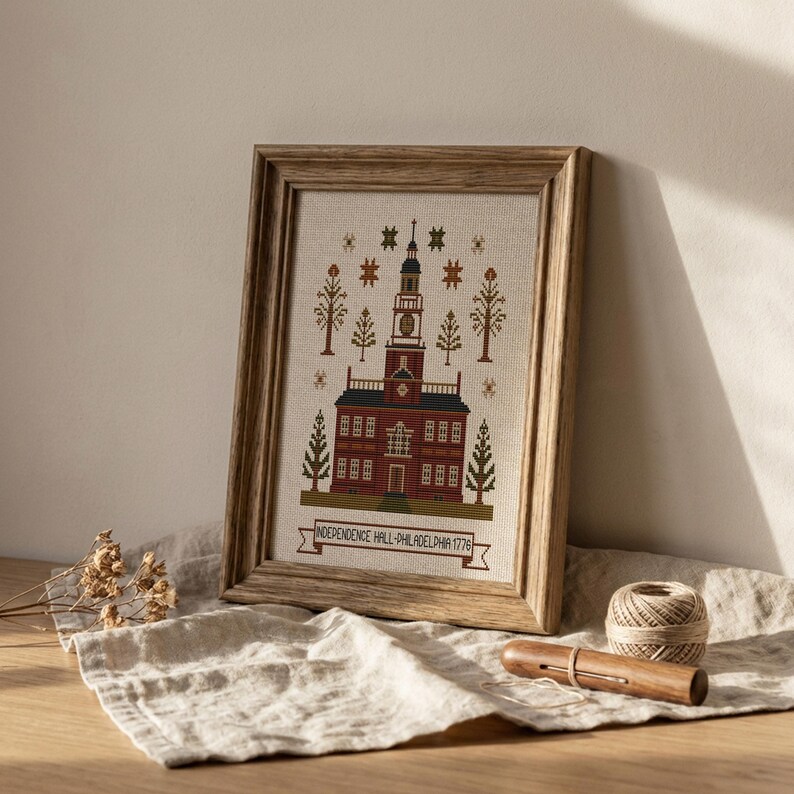 May include: A framed cross-stitch of Independence Hall in Philadelphia, Pennsylvania, with a wooden frame. The building is red brick with a white clock tower. The text "INDEPENDENCE HALL-PHILADELPHIA 1776" is below the building.
