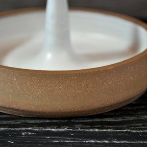 May include: A brown ceramic ring holder with a white center. The holder has a speckled texture.