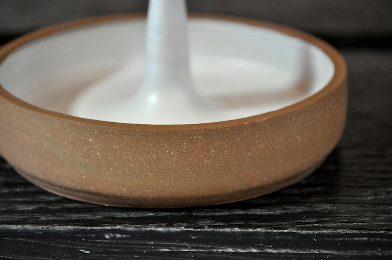 May include: A brown ceramic ring holder with a white center. The holder has a speckled texture.