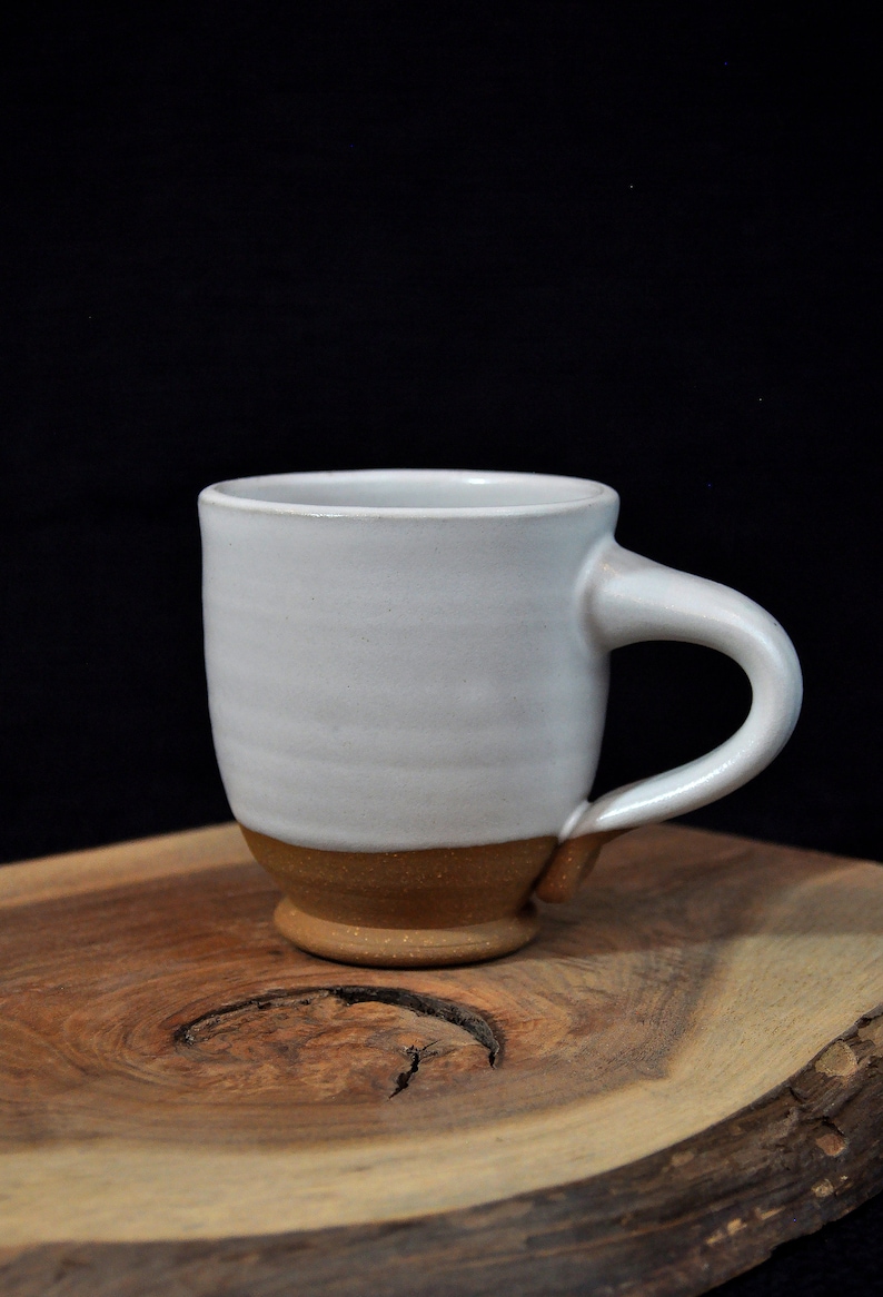 May include: A white ceramic mug with a brown rim and a handle. The mug is sitting on a wooden surface.
