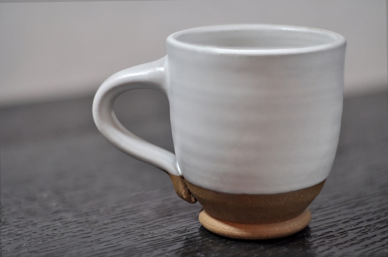 May include: A white ceramic mug with a brown rim and base. The mug has a simple, rounded design and a comfortable handle.