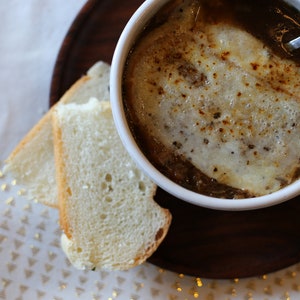 Puede incluir: Un taz&oacute;n de sopa de cebolla francesa con queso derretido encima, servido con dos rebanadas de pan.