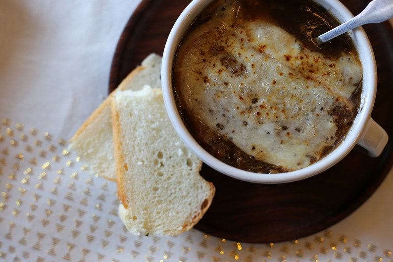 Puede incluir: Un taz&oacute;n de sopa de cebolla francesa con queso derretido encima, servido con dos rebanadas de pan.