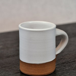May include: A white ceramic mug with a brown clay base. The mug has a rounded handle.