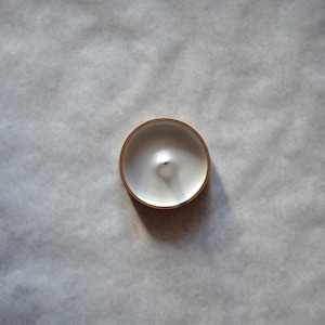 May include: A white candle in a round, gold-rimmed container.