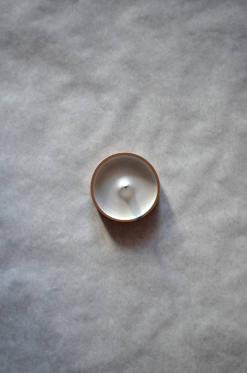 May include: A white candle in a round, gold-rimmed container.