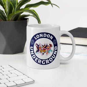May include: White ceramic mug featuring a London Underground logo. The logo is a circular design with the words "LONDON UNDERGROUND" in navy blue, encircling a colorful map of the tube lines.