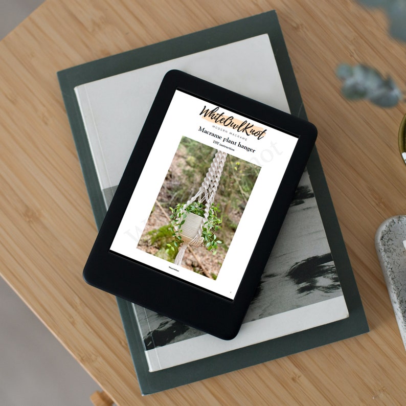 May include: A digital tablet displaying a printable macrame plant hanger pattern from White Owl Knot. The pattern includes instructions for a macrame plant hanger with a white cord and a potted plant.