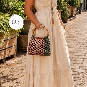 May include: A macrame handbag featuring a circular bamboo handle and a two-toned knotted cord design in dusty pink and olive green. The bag has a structured, open-weave pattern and is held by a person wearing a long, light beige linen dress.