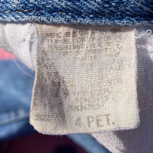 Puede incluir: Una etiqueta de tela blanca con texto negro que dice "100% PET."
