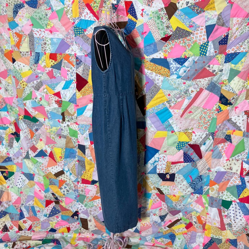 May include: A sleeveless, denim blue dress with a scoop neckline. The dress is displayed on a wire dress form. The background is a colourful patchwork quilt with various fabric patterns and colours.