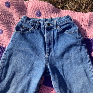 Puede incluir: Un par de pantalones vaqueros azules de cintura alta con cierre de bot&oacute;n y cinco bolsillos.
