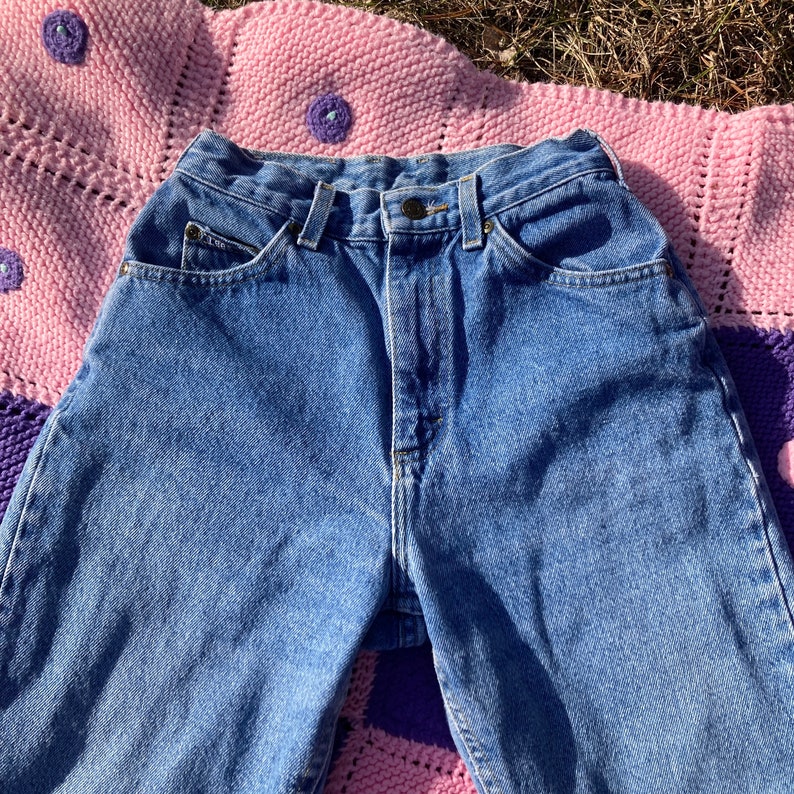 Puede incluir: Un par de pantalones vaqueros azules de cintura alta con cierre de bot&oacute;n y cinco bolsillos.