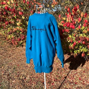 May include: A blue Champion sweatshirt with a black embroidered logo on the front.