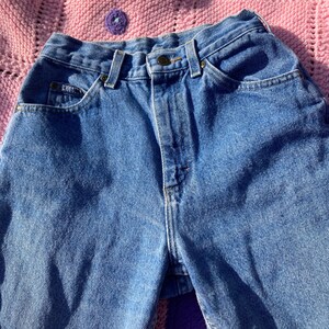 Puede incluir: Un par de pantalones vaqueros azules de cintura alta con cierre de bot&oacute;n y cinco bolsillos.