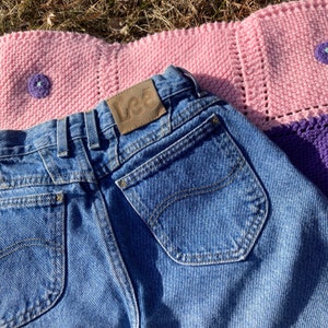 Puede incluir: Un par de pantalones vaqueros azules con un parche de cuero marr&oacute;n que dice "Lee" en la parte posterior. Los vaqueros tienen un bolsillo trasero con un dise&ntilde;o cosido.