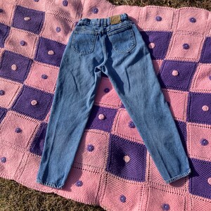 Puede incluir: Un par de pantalones vaqueros azules de mezclilla de cintura alta y pierna recta. Los vaqueros tienen un logotipo de Lee en el bolsillo trasero.