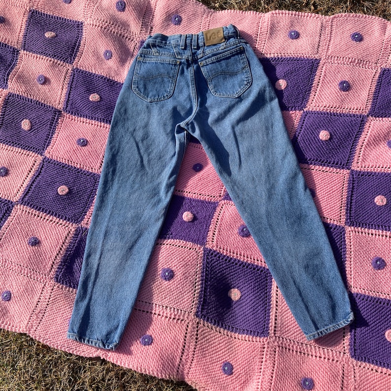 Puede incluir: Un par de pantalones vaqueros azules de mezclilla de cintura alta y pierna recta. Los vaqueros tienen un logotipo de Lee en el bolsillo trasero.