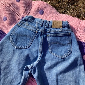 Puede incluir: Un par de pantalones vaqueros azules con un parche de cuero marr&oacute;n que dice "Lee" en la parte posterior. Los pantalones tienen dos bolsillos traseros y un ajuste cl&aacute;sico.