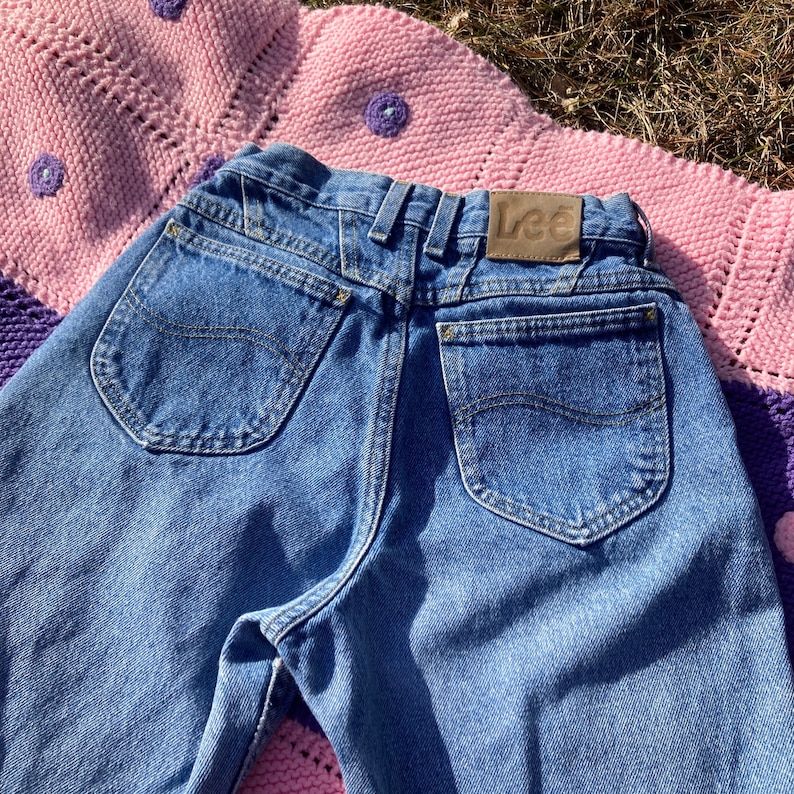 Puede incluir: Un par de pantalones vaqueros azules con un parche de cuero marr&oacute;n que dice "Lee" en la parte posterior. Los pantalones tienen dos bolsillos traseros y un ajuste cl&aacute;sico.