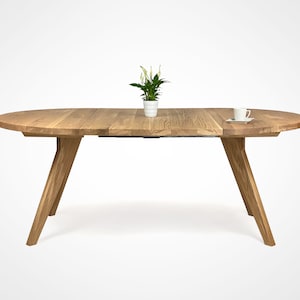 table with a massiv round top and four slanted legs, which taper downwards. On the top there is a flower in a white pot and a cup. the table has a unique grain pattern, typical of natural wood. the table is shown with two extensions.