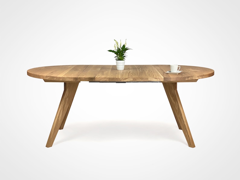 table with a massiv round top and four slanted legs, which taper downwards. On the top there is a flower in a white pot and a cup. the table has a unique grain pattern, typical of natural wood. the table is shown with two extensions.