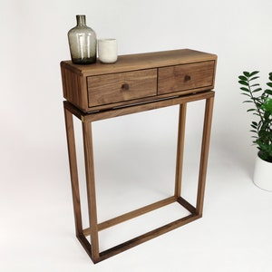 Op de afbeelding: Een consoletafel van walnoot hout met twee laden en een lager open rek. De tafel heeft een modern ontwerp met een eenvoudig, rechthoekig frame en messing beslag.
