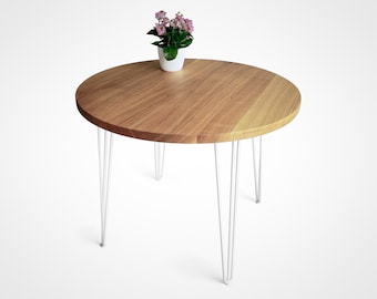 Puede incluir: Una mesa redonda de madera con un acabado de madera natural y patas de horquilla blancas. Una pequeña planta en maceta con flores rosas se encuentra sobre la mesa.