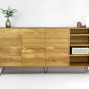 Op de afbeelding: Een licht houten dressoir met vier lades en twee deuren aan de linkerkant en open planken aan de rechterkant. Het dressoir heeft zwarte haarspeldpoten.