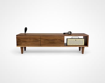 May include: A mid-century modern style walnut wood entertainment console with two drawers and an open shelf. The console has a light brown finish and is sitting on four tapered legs. A small amplifier is sitting on the shelf.