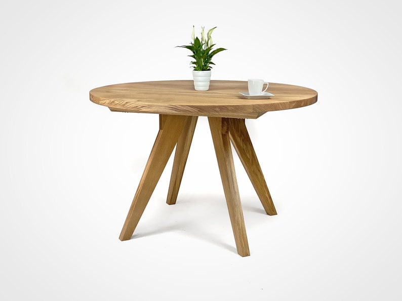 table with a massiv round top and four slanted legs, which taper downwards. On the top there is a flower in a white pot and a cup. the table has a unique grain pattern, typical of natural wood. the table is shown in a folded version.