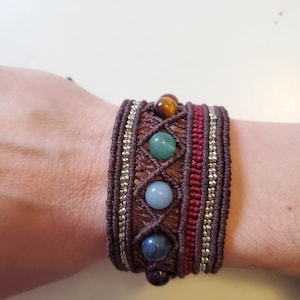 May include: A brown bracelet with a woven design and colorful gemstone beads. The beads are red, orange, green, blue, and purple.