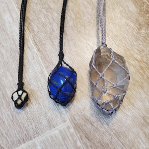 Peut inclure: Trois colliers en cristal avec des pierres de différentes couleurs. Les colliers sont faits de ficelle noire, grise et blanche. Les pierres sont un lapis-lazuli bleu, un quartz clair et une pierre blanche.